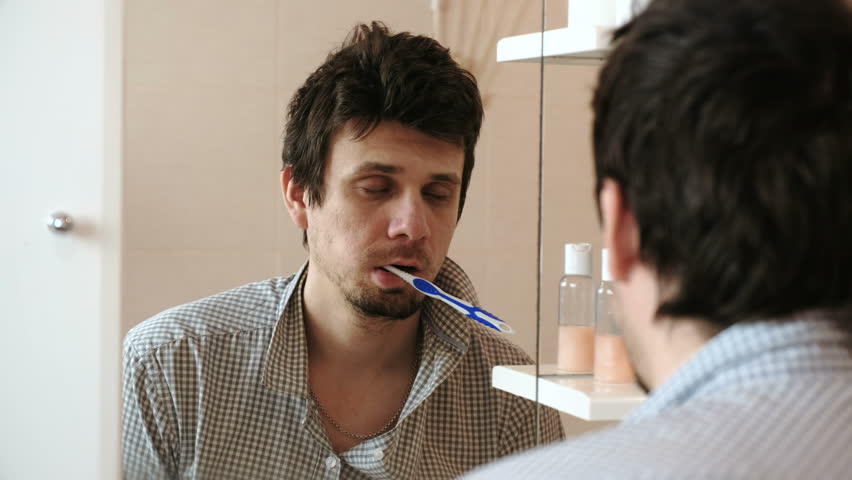 Tired sleepy man with a hangover who has just woken up brush his teeth, looks at his reflection in the mirror. Royalty-Free Stock Footage #1012974551