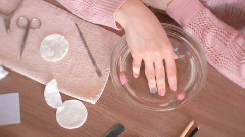 Manicure at home. Woman dipping her hand in a bowl of water. Hand close-up, manicure tools on the table. Top view.