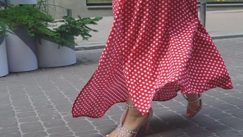 female feet in beige sandals with heels with rivets go along the road. A woman in a red dress with polka dots. Slow motion.