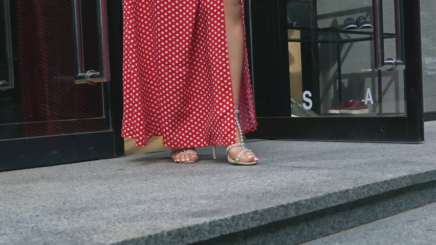 female feet in beige sandals with heels with rivets descend the stairs. Stairs of the boutique. A woman in a red dress with polka dots. Slow motion.