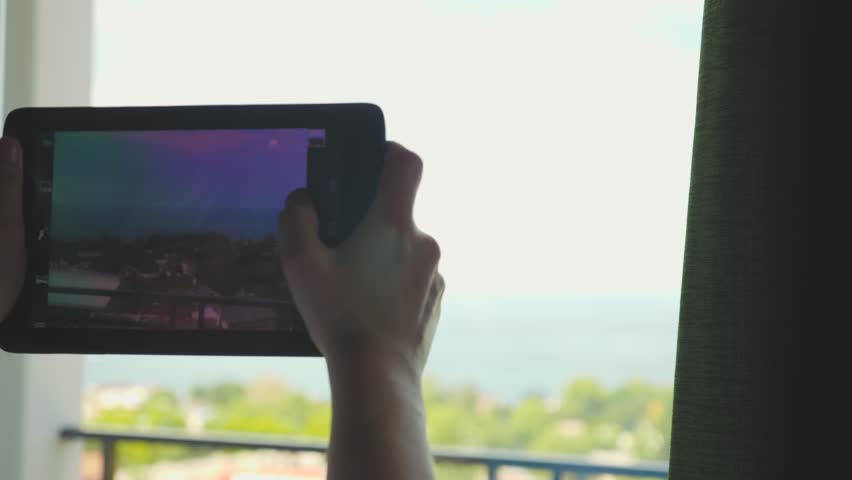 A young girl with blonde using a tablet takes pictures and videos of the landscape outside the window. Royalty-Free Stock Footage #1012980320