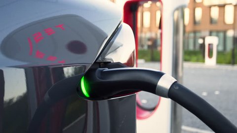 AMSTERDAM, NETHERLANDS, circa June 2018. Male hand plugs off the charging cable from a Tesla Model X electric car, in a newly build Tesla super charging station. Tesla logo reflecting on the car.