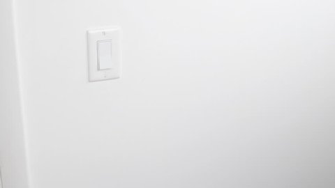 Flat white panel light switch on a white wall being turned on and off by a caucasian male hand closeup. White flat plastic light switch control on a wall being turned on and off by a mature adult man