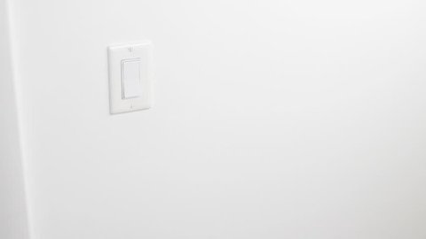 Flat plastic white light switch panel being turned on and off by an adult caucasian male hand and forearm. Interior control panel to turn on an overhead light being turned on and off by a hand closeup