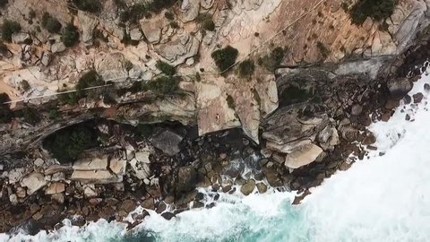 An aerial footage zooming out on a couple laying down on the cliff by the coast and sea.