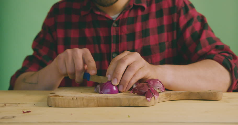 A youn gman is chopping onions against a green screen