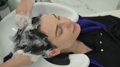 Beauty procedures, hairdresser cares for girl client hair with shampoo at barbershop close-up