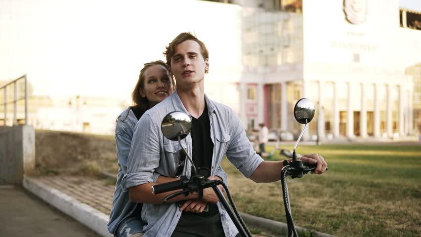 Overview footage of a beatuful couple sitting on a bike. Girl is hugging man from the back. Wearing black T shirt and blue shirt. Summer day