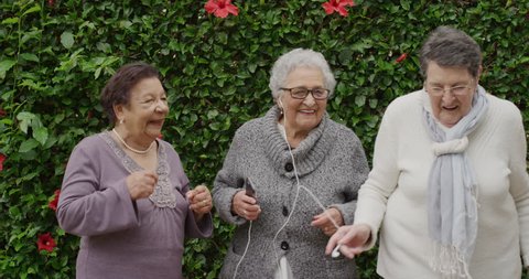 portrait of diverse senior women dancing happy enjoying celebrating retirement listening to music together in outdoors gardenの動画素材