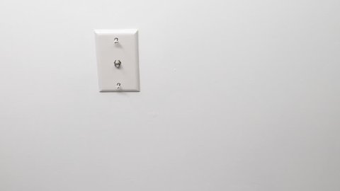 One male caucasian hand screwing in with a screwdriver a white wall outlet for cable television closeup. Mature male hand and arm tightening upper and lower screws for a cable outlet on a white wall.