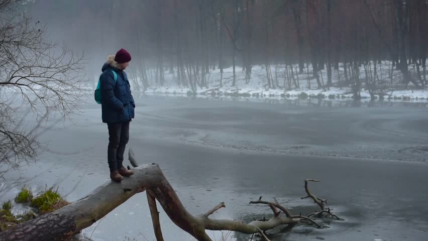 man standing on fallen tree near the river in foggy winter landscape