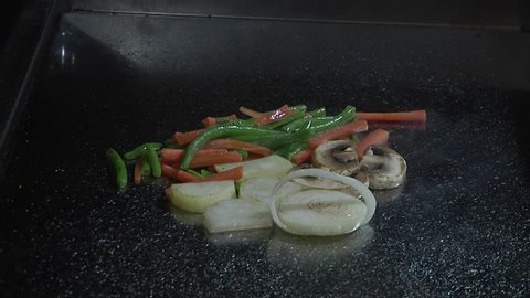 Close up of steaming vegetables being grilled on a Teppanyaki grill at restaurant with sauce