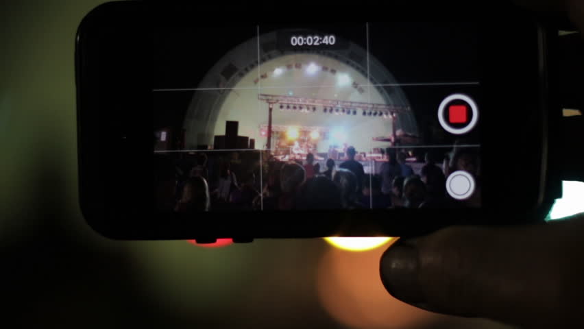 Recording a concert with a smart phone at a music festival with a live band playing. Close up of a cell phone recording live video of a band. 