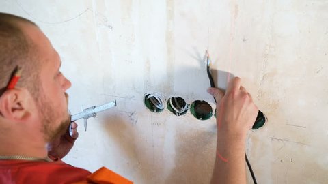 Closeup electrician checking technical parameters with calipers on building site. Worker control distance accuracy between installed wiring junction box on concrete wall. Safety policy, repair concept