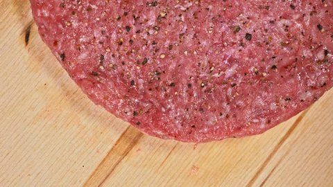 Cook makes meat medallions for burgers. Chef in black food gloves makes cutlet. Cutlets are leveled in steel ring in an even medallion. On top of pouring spices pepper and salt. Meat marbled beef lies