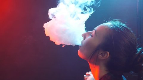Young woman in bright lights with colorful smoke. Smoking electronic cigarettes concept