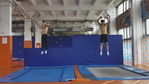 Two gymnasts jumping synchronously on trampolines, slow motion. Symmetry.