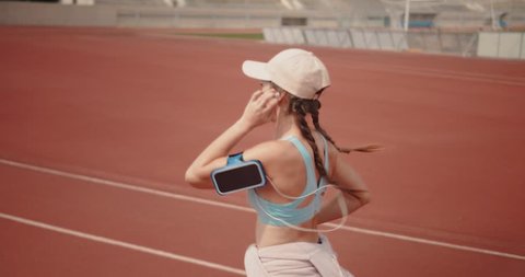 Young athletic woman doing sports practice by running on sports track and listening to music