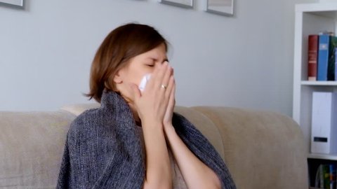 Woman sitting on a sofa, feeling ill and sneezing