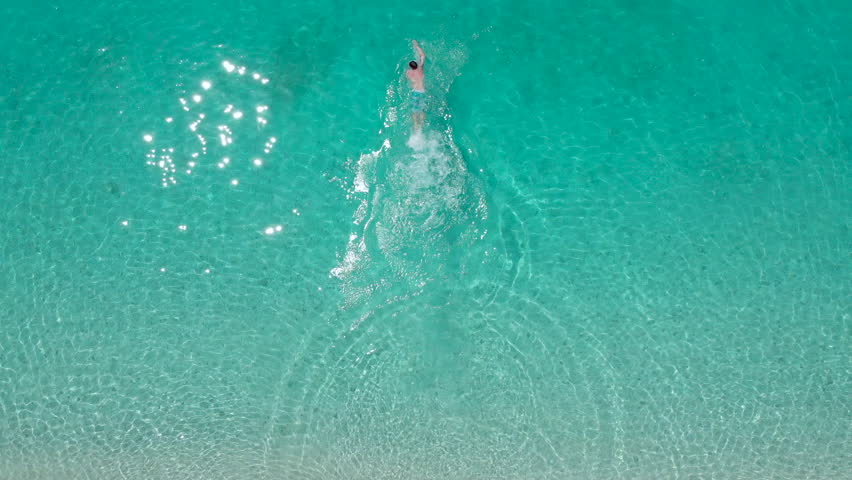 Aerial - Top down view of adult man running into turquoise color water