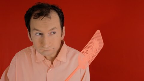 A funny ugly man trying to squash a fly with a swatter, but ending up hitting himself on the head. Red background.
