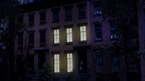 A nighttime exterior establishing shot of a typical Brooklyn brownstone residential row house. Window lights turn on and off. Simulated day-for-night treatment. Day/Night matching available.
