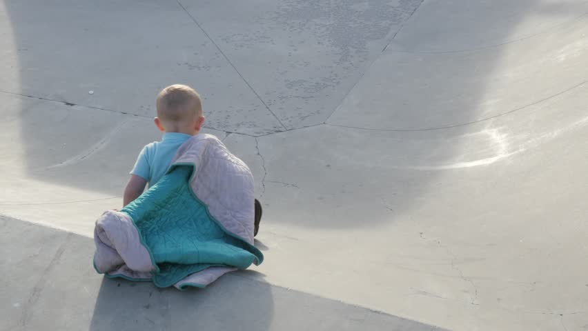 Baby boy sliding down cement skate park with his blanket.
