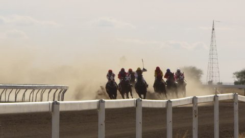 A medium shot of horse riding in slow motion creating smoke on their trail. Camera pans to the left.