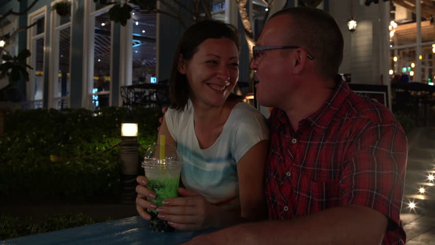 A woman and a man are drinking Bubble Tea while sitting at a table in the street and kissing