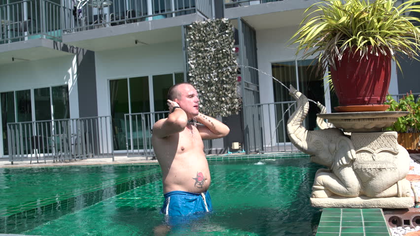 A man stands in the pool under the stream of water flowing out of the trunk of a stone elephant