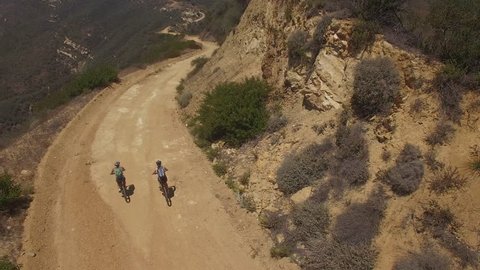 Aerial of cyclists riding along dirt road on the cliff of a mountain - Βίντεο στοκ