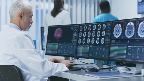 Experienced Senior Scientist Working with CT/ MRI Brain Scan Images on a Personal Computer in Laboratory. Neurologists / Neuroscientists in Medical Research Center. Shot on RED EPIC-W 8K Helium Camera