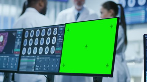 Computer Monitors Showing Green Mock-up Screen, MRI, CT Image Scans of the Brain. In the Background Meeting of the Team of Medical Scientists in the Brain Research Laboratory. Shot on RED EPIC-W 8K.