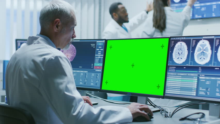Senior Medical Research Scientist Working with Brain Scans on His Personal Computer Showing Green Mock-up Screen. Modern Laboratory Working on Neurophysiology. Shot on RED EPIC-W 8K Helium Cinema Came