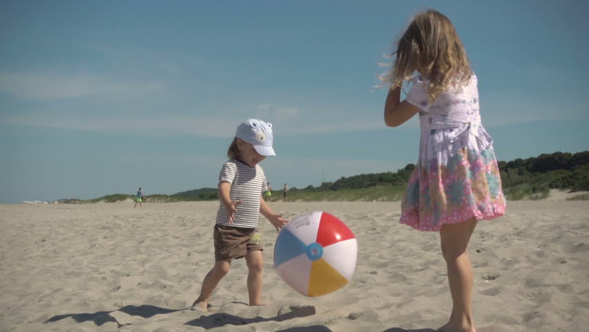 Children playing on the beach. Family Summer Beach Vacation. Slow Motion. Happy boy and girl child play a ball at coast on a sunny summer day