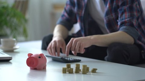 Man calculating money, putting coins into piggy bank, family budget planning