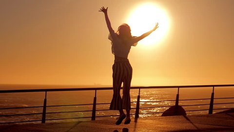 Active young woman silhouette dancing outdoors on a sunset with sun shining bright behind her on a horizon. Slow motion