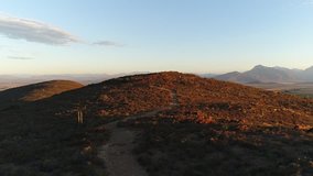 Wide aerial shot of a man running on a dirt path up a mountain in South Africa at sunset