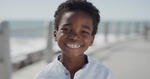 close up portrait happy african american boy smiling cheerful enjoying warm summer vacation on seaside beach waterfront slow motion