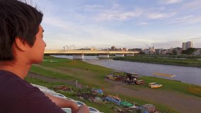 Young JAPANESE MAN looking at the river and thinking of something.  At sunset riverside of Tama river in Tokyo.