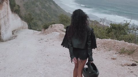 Back view of beautiful woman motorcycle rider walking with helmet near amazing limestone cliffs over sea  background - video in slow motion