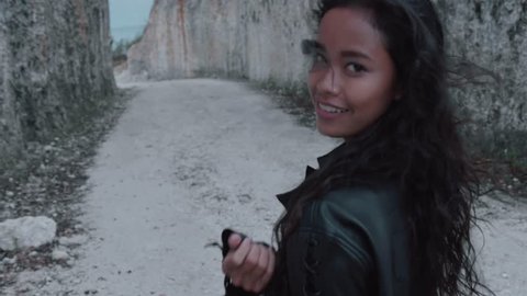 Beautiful happy woman motorcycle rider walking with helmet near amazing limestone cliffs. Girl getting over stile and gesturing come along follow me - video in slow motion