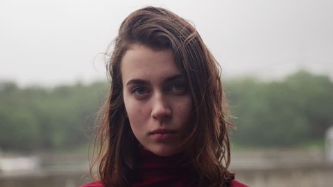 Close-up face of young woman with sad look and wet hair in rain, cloudy bad weather