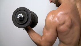 Slow motion closeup video of a shirtless muscular man training biceps with dumbbell