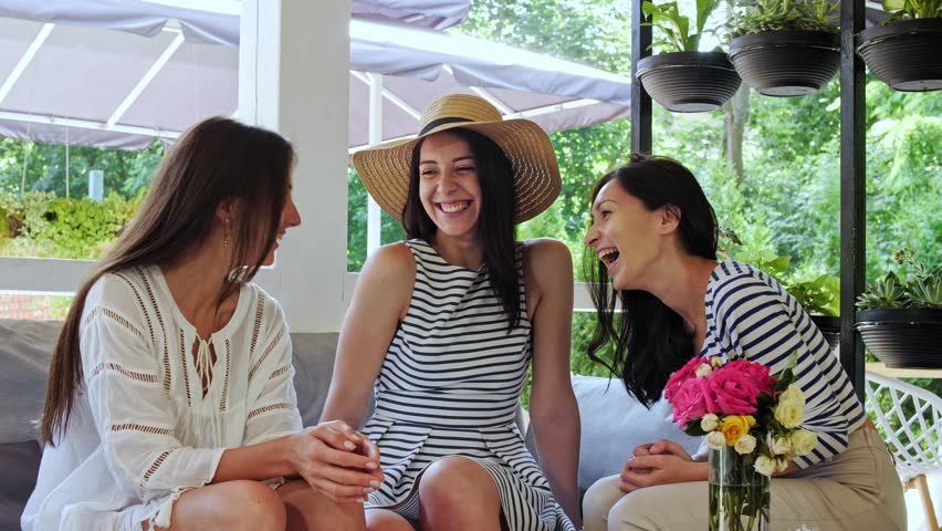 Three cheerful girls are chatting and having fun during sitting at cafe