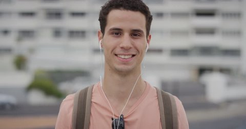 portrait handsome young hispanic man student smiling enjoying listening to music wearing earphones in city slow motion