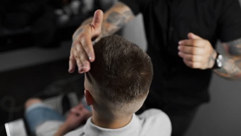 Tattoed barber makes hair styling with hair gel for customer after haircut at the barber shop, man's haircut and shaving at the hairdresser, barber shop and shaving salon