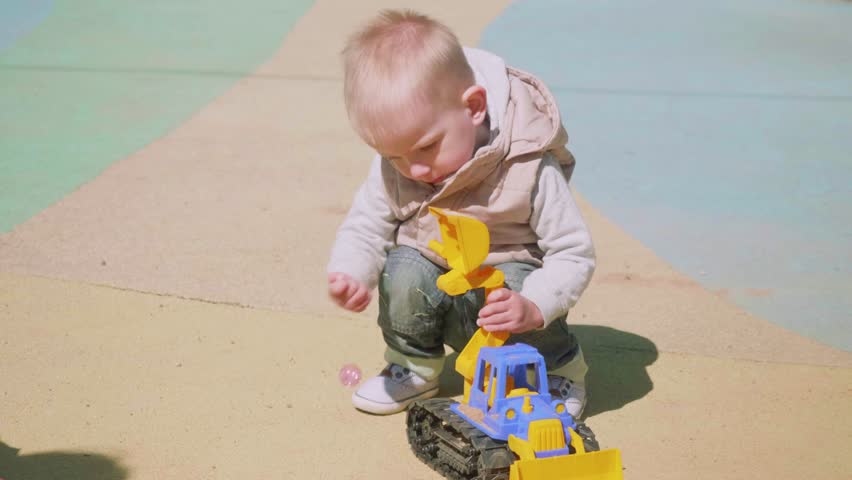 Blond toddler plays with toy tractor on playground