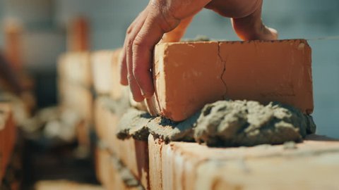 The builder's hand puts the brick in the masonry of the wall.