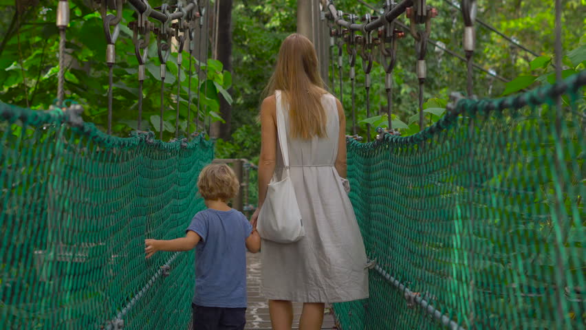 Steadicam shot of a young woman and her son walking on the hanging suspension bridge in the Eco Park in the Kuala Lumpur city